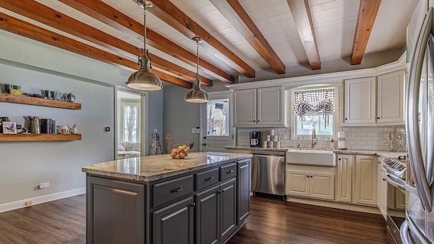 A kitchen with dark cabinets, a large island, wooden beams on the ceiling, and a window with a view. - The 1840's Goat House (Elburn)