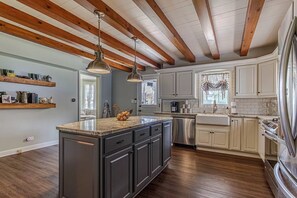 A kitchen with dark cabinets, a large island, wooden beams on the ceiling, and a window with a view. - The 1840's Goat House (Elburn)