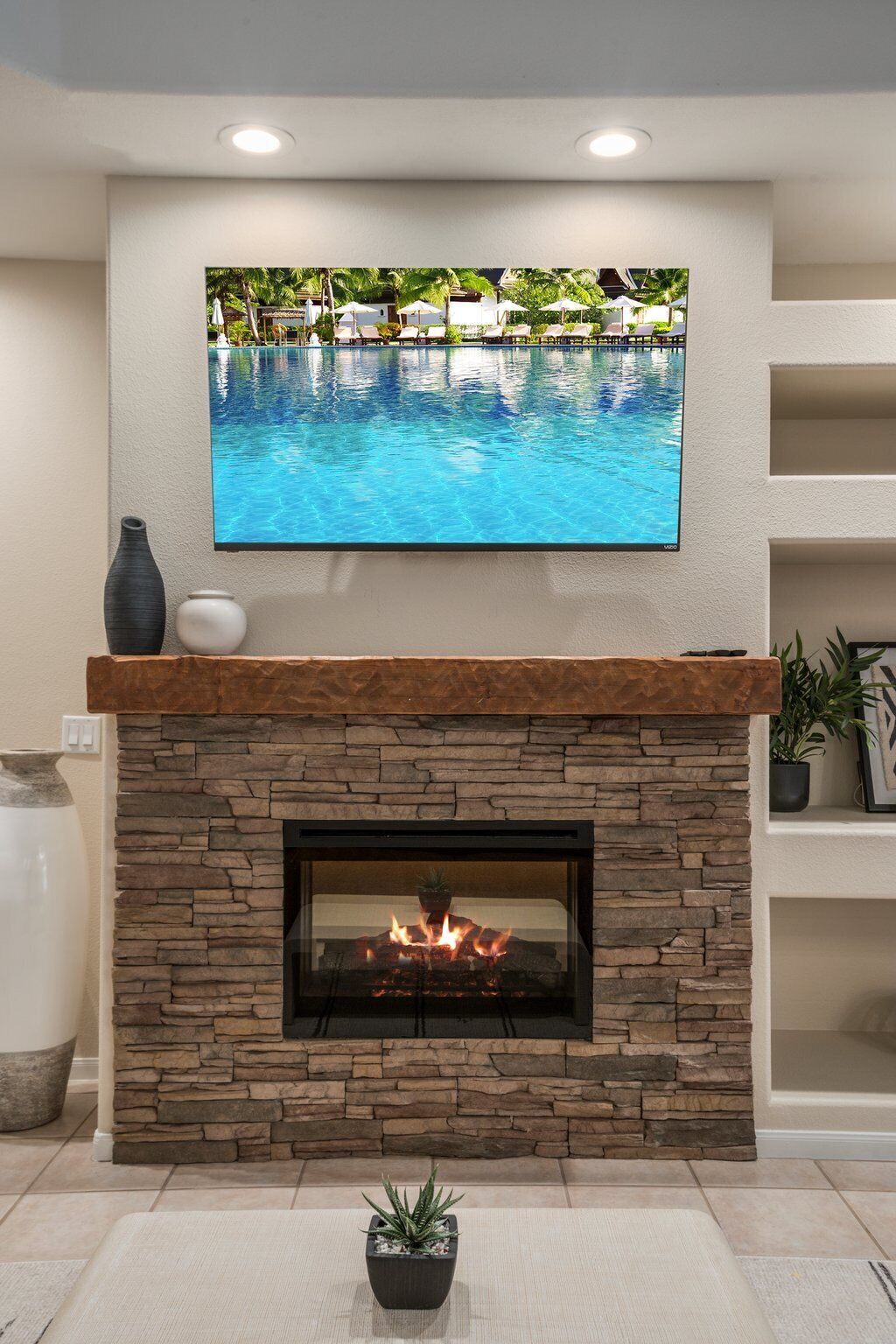 A living room with a stone fireplace, a flat-screen TV above it, and a potted plant on the floor.