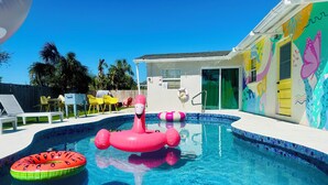 Una piscina amb joguines inflables, una zona de porxo coberta i un mural de paret colorit.