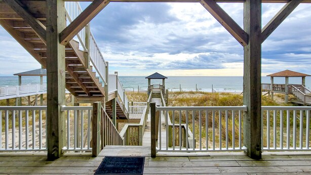 Eine Holzterrasse mit Blick auf Strand und Meer.
