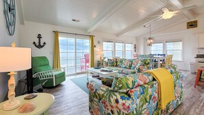 Ein geräumiges Wohnzimmer mit großem Fenster, Deckenventilator und farbenfroher Couch.