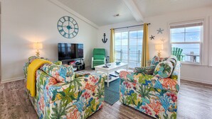 Ein Wohnzimmer mit einer großen Uhr, einem grünen Sessel und einer Couch mit bunten Blumenmuster.