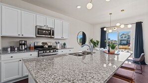 Una cocina moderna con armarios blancos, encimeras de granito, electrodomésticos de acero inoxidable y una isla grande con taburetes de bar.