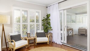 Een gezellige kamer met rieten meubels, een grote plant en een uitzicht door een schuifdeur op een terras.