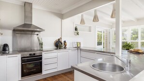 Een moderne keuken met witte kastjes, roestvrijstalen apparatuur en hangende lampen.