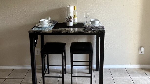 Un comedor con una mesa dispuesta para dos personas, un cuadro en la pared y una planta en maceta sobre la mesa.