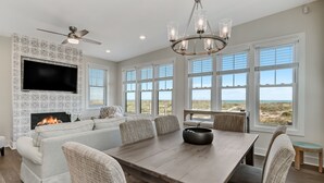 A modern living room with a fireplace, large windows, and a dining area. - 2100 South Fletcher - Beautifully Updated, Oceanfront Bungalow (Fernandina Beach)