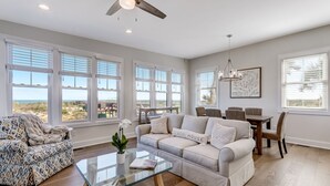 A spacious living room with a large window, a ceiling fan, and a dining area with a table and chairs. - 2100 South Fletcher - Beautifully Updated, Oceanfront Bungalow (Fernandina Beach)