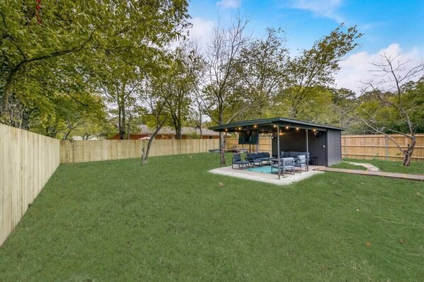 Un jardin avec un patio couvert, une piscine et une clôture en bois.