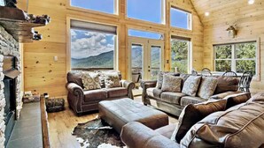 A cozy cabin interior with wooden walls, large windows, a fireplace, leather sofas, and a deer head decoration. - One-of-kind Views! Stunning Sunsets! Highly Sought after Location! (Marion)