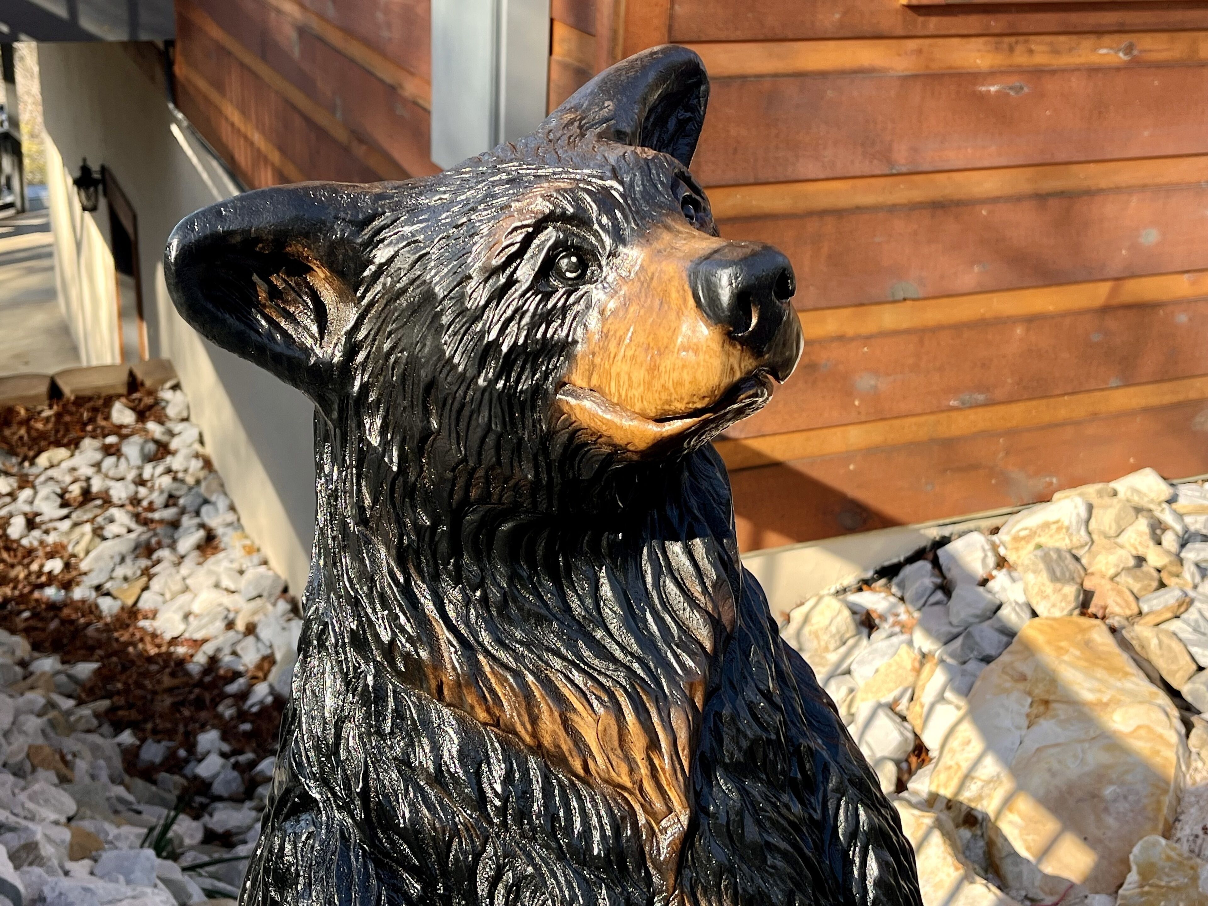A wooden bear statue outdoors with a house in the background.