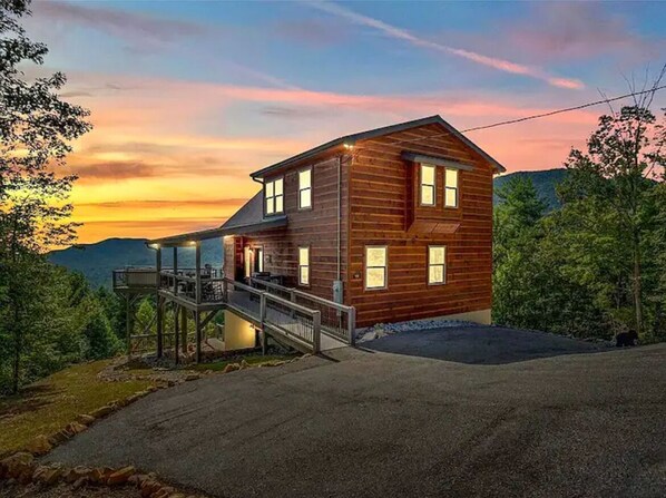 Een houten vakantiehuis met twee verdiepingen en een balkon, voor een zonsondergang.