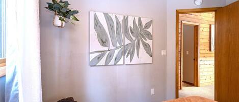 A bedroom with a bed, a hanging plant, and a wall art piece.