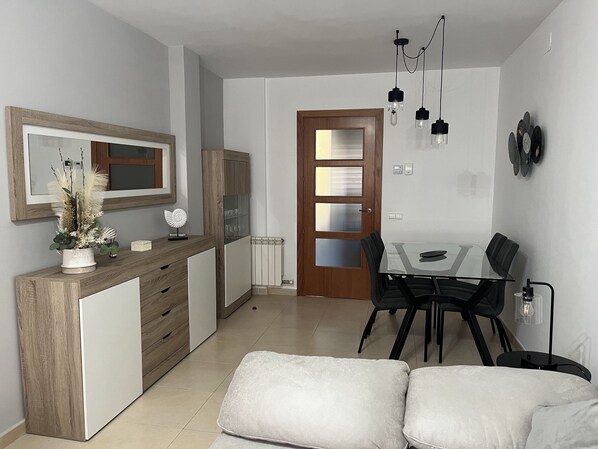 A modern kitchen with a wooden cabinet, a dining table with chairs, and a white sofa. - Holiday Apartment Near Sitges With Private Terrace (Vilanova i la Geltrú)