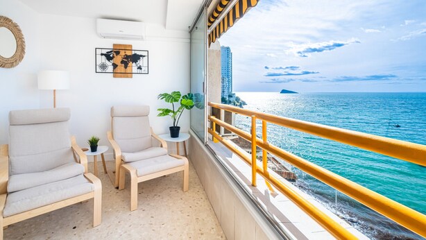 Ein Balkon mit zwei Stühlen, einem kleinen Tisch, einem Blumentopf und Blick aufs Meer.