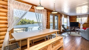 Interno di una baita in legno con un tavolo da pranzo, panche, una televisione e vista su un lago.