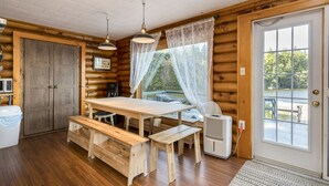 Interno di una baita in legno con un tavolo da pranzo in legno, panche, un condizionatore bianco e una porta che dà sull'esterno.