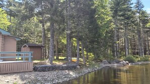 Una baita con veranda che si affaccia su un lago limpido, circondata da alberi alti.