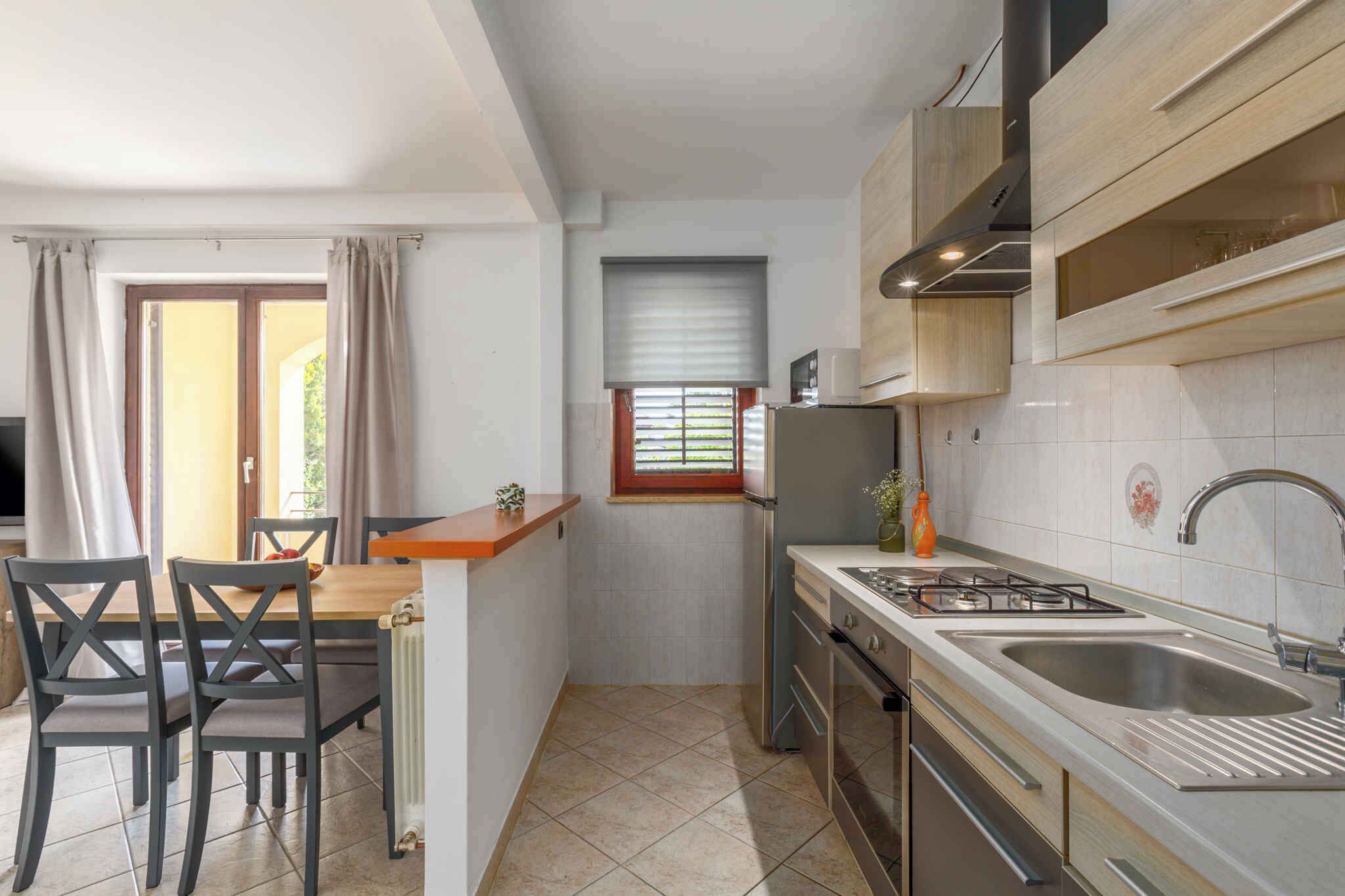 A compact kitchen with a dining area, a window with blinds, and a built-in oven.