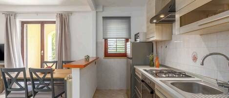 A compact kitchen with a dining area, a window with blinds, and a built-in oven.
