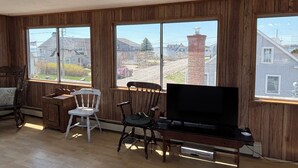 Une pièce aux murs en bois, un téléviseur posé sur un meuble en bois et deux chaises.