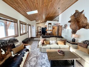 A cozy living room with a large leather sofa, a coffee table with pinecones, and a rustic ceiling. - NEW! LAST MIN SPECIAL! Ski Chalet, Spacious, Clean, Close To Everything! (Big Sky)