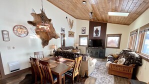 A cozy living room with a wooden ceiling, a dining area with a wooden table and chairs, and a sofa with a fur throw. - NEW! LAST MIN SPECIAL! Ski Chalet, Spacious, Clean, Close To Everything! (Big Sky)