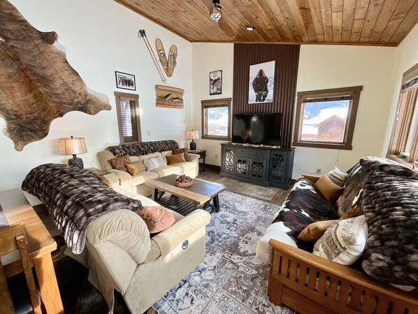 A cozy living room with a large fur rug, a wooden coffee table, and a fireplace. - NEW! LAST MIN SPECIAL! Ski Chalet, Spacious, Clean, Close To Everything! (Big Sky)
