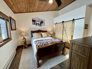 A bedroom with a wooden bed, a nightstand with a lamp, a wardrobe, and a wall-mounted curtain rod. - NEW! LAST MIN SPECIAL! Ski Chalet, Spacious, Clean, Close To Everything! (Big Sky)