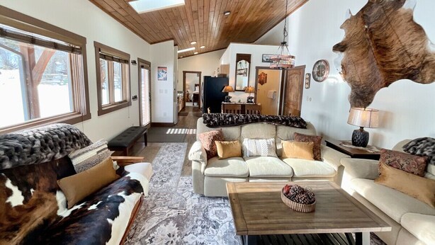 A cozy living room with a large wooden ceiling, a cowhide wall hanging, and a rustic coffee table. - NEW! LAST MIN SPECIAL! Ski Chalet, Spacious, Clean, Close To Everything! (Big Sky)