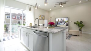 A modern kitchen with stainless steel appliances, a large island, pendant lights, and a view of a residential area. - 2024 Unique Villa 5 min to Disney (Kissimmee)