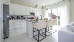 A modern kitchen with white cabinets, stainless steel appliances, and a central island with bar stools. - 2024 Unique Villa 5 min to Disney (Kissimmee)