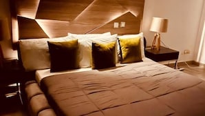 A modern bedroom with a geometric-patterned headboard, a large bed with multiple pillows, and a bedside table with a lamp. - Granville Penthouse Apartments (Lekki)