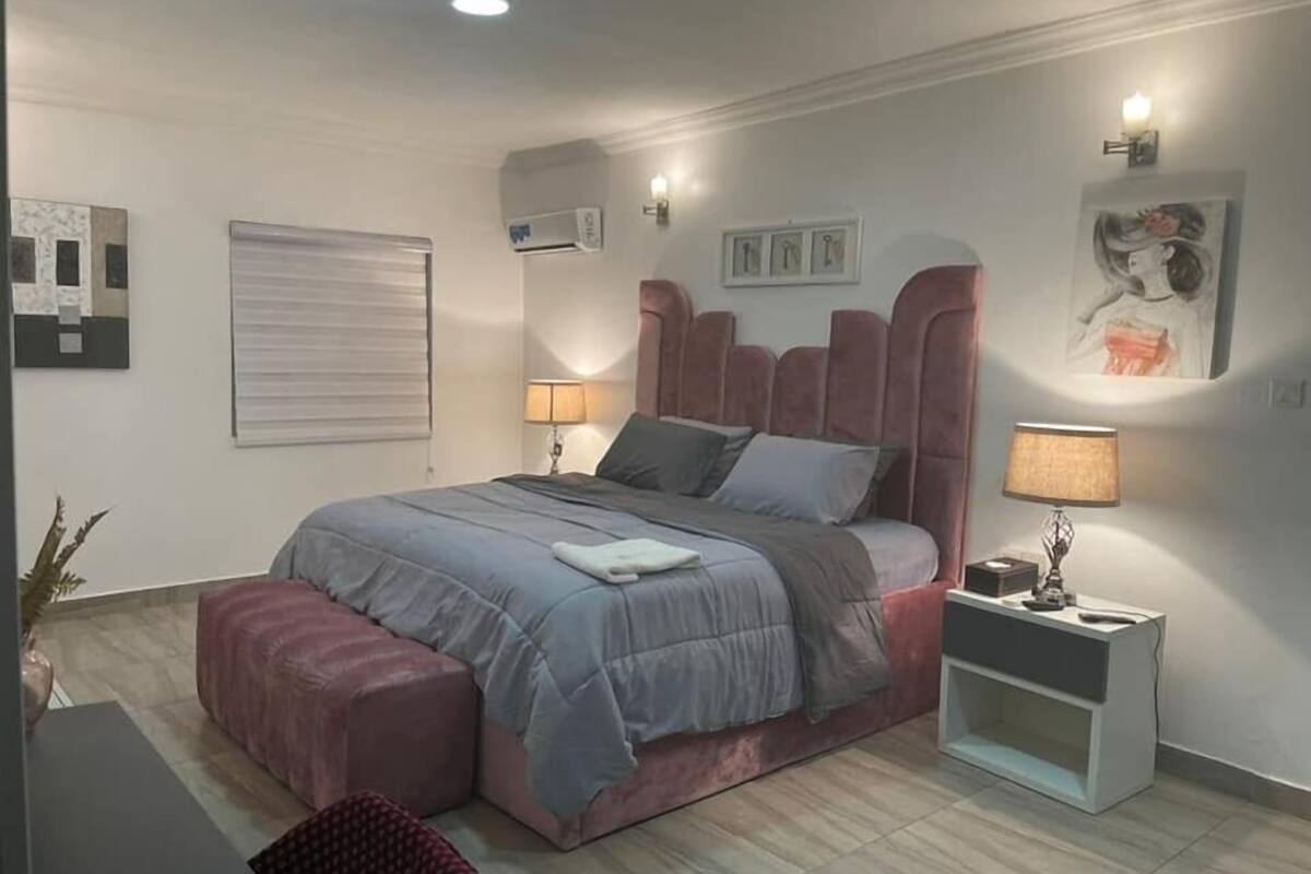 Une chambre moderne avec un grand lit, une table de chevet, une lampe et un climatiseur fixé au mur.