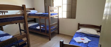 Um dormitório com beliches, uma janela com persianas e uma porta.
