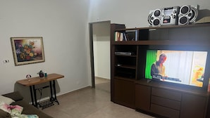 A living room with a brown sofa, a small wooden table, a TV on a wooden stand, and a framed picture on the wall.