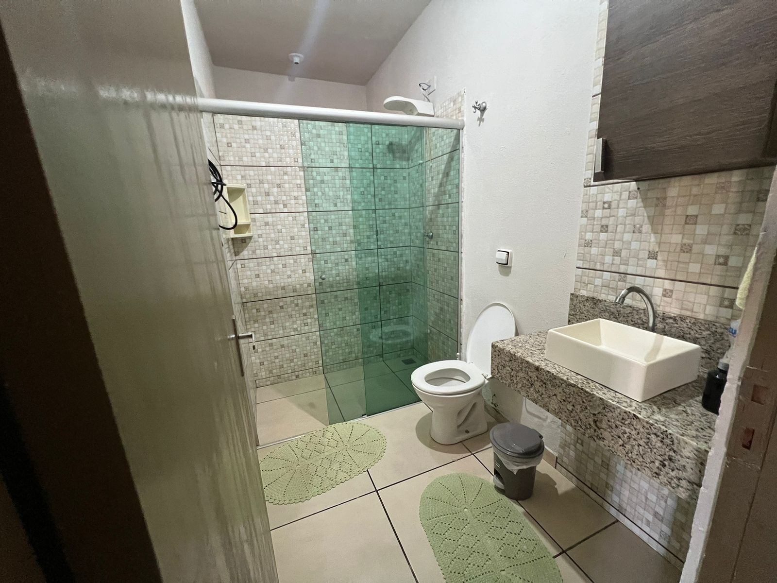 A bathroom with a shower, toilet, sink, and a small trash bin.