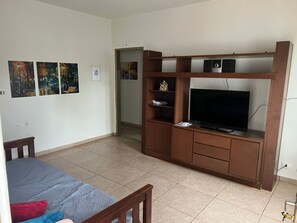 A room with a bed, a wooden entertainment unit with a TV, and three paintings on the wall. - Hostel Jotaaa F (Ourinhos)