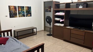 A bedroom with a bed, a bench, a TV, a fan, and a wardrobe.