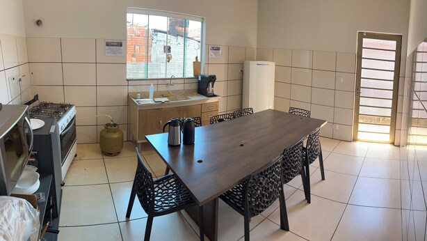 A kitchen with a gas stove, sink, and coffee maker. There is a dining table with chairs and a window with blinds.