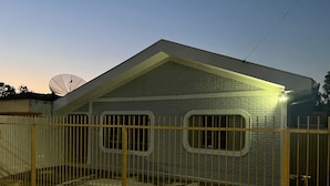 A single-story house with a sloped roof, a satellite dish, and a fenced yard.
