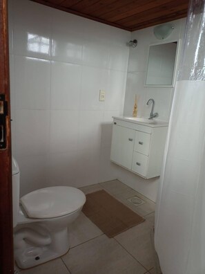 A small, clean bathroom with white tiles, a toilet, a sink with a mirror, and a shower curtain.