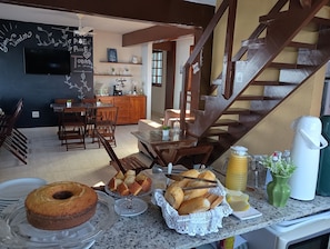 A kitchen with a dining area, wooden staircase, and a chalkboard with writing. - HOSTEL GUARATIBA CASA DO CAFÉ (Rio de Janeiro)