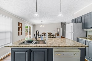 Una cocina con encimeras de granito, lavavajillas integrado, refrigerador y comedor con mesa y sillas.