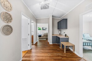 A hallway with wooden flooring, a bench, and a kitchen area with cabinets and a countertop.