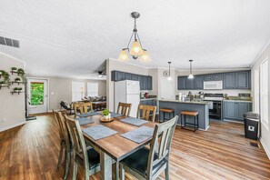 A modern kitchen with wooden flooring, a dining area with a wooden table and chairs, and a small island with bar stools.