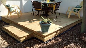 Eine Holzterrasse mit Tisch und Stühlen, einem Blumentopf und einem blauen Sonnenschirm.