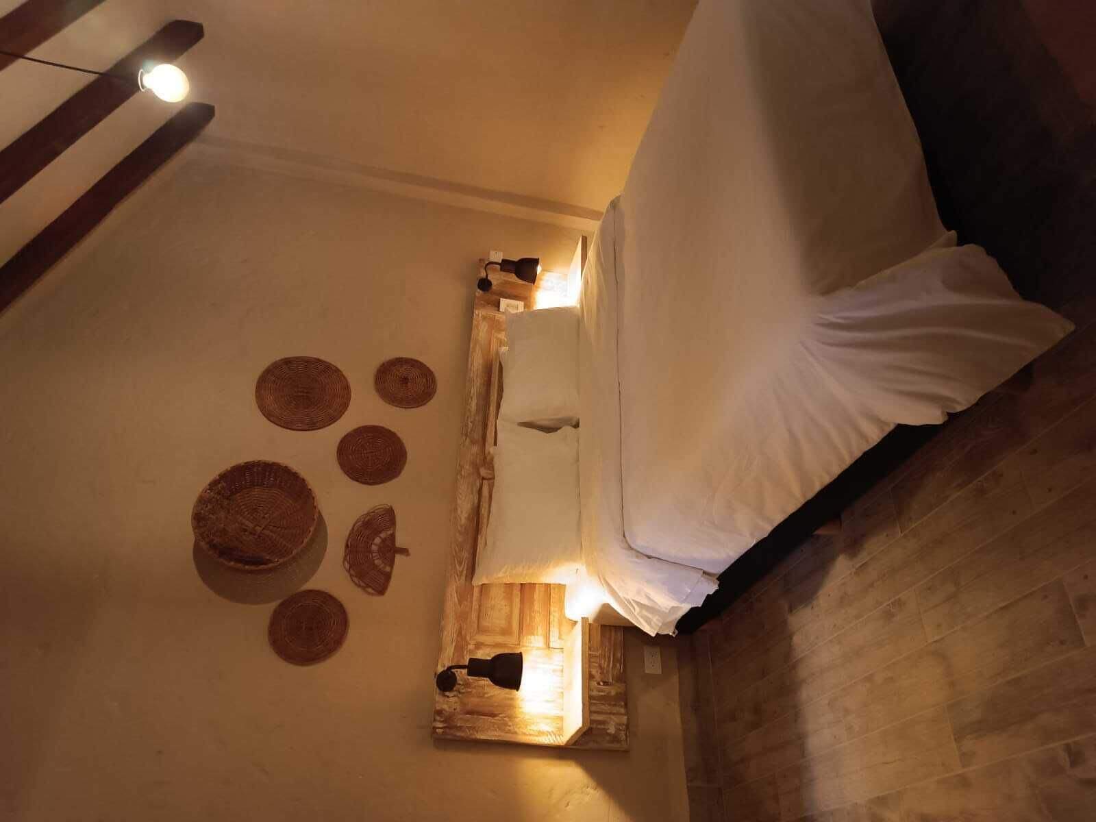 Et værelse med en seng, et træsengegavl, en vægmonteret lampe og vægpynt i vævet materiale.