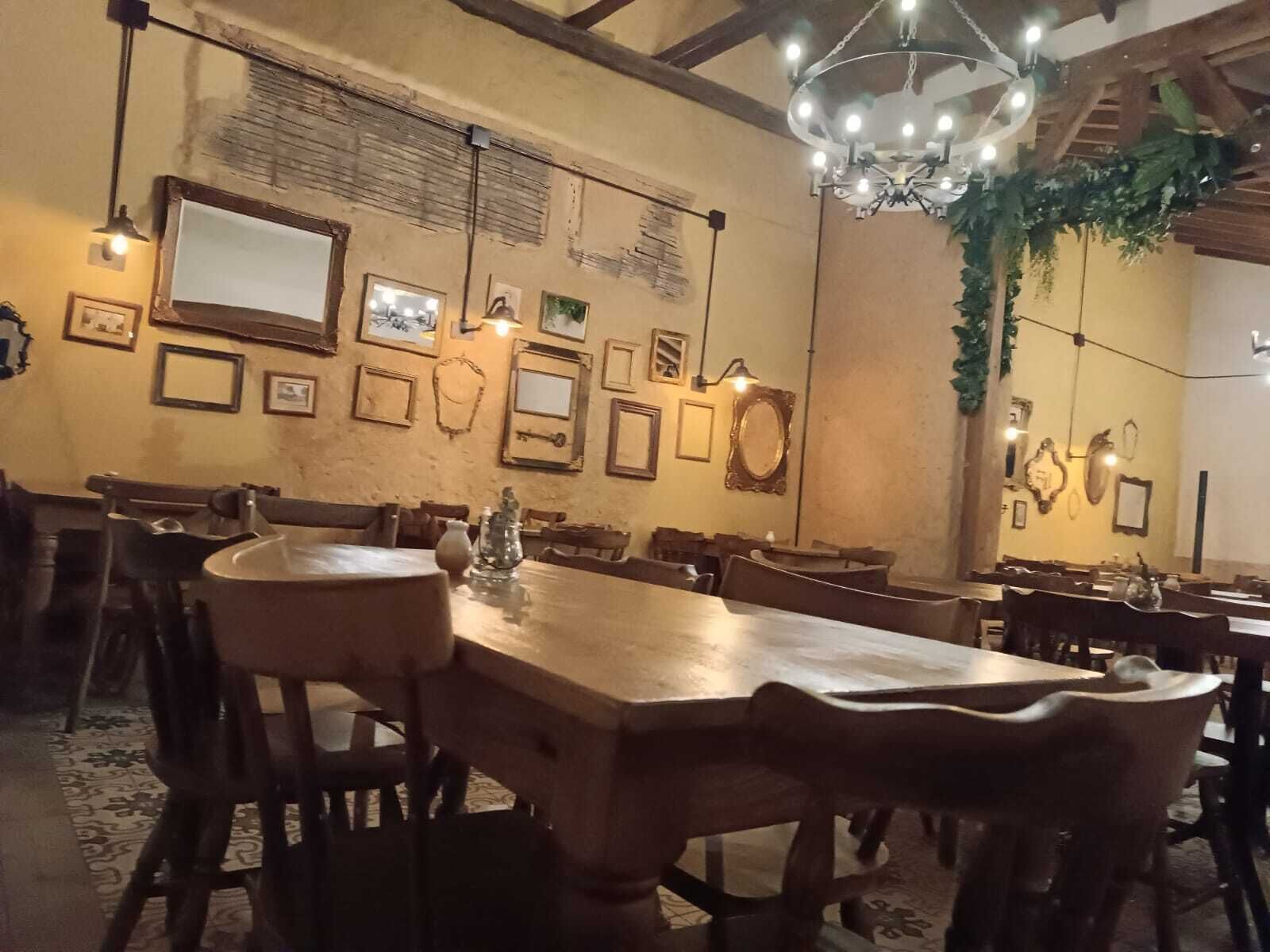 A dining area with wooden tables and chairs, framed pictures on the walls, and a chandelier.